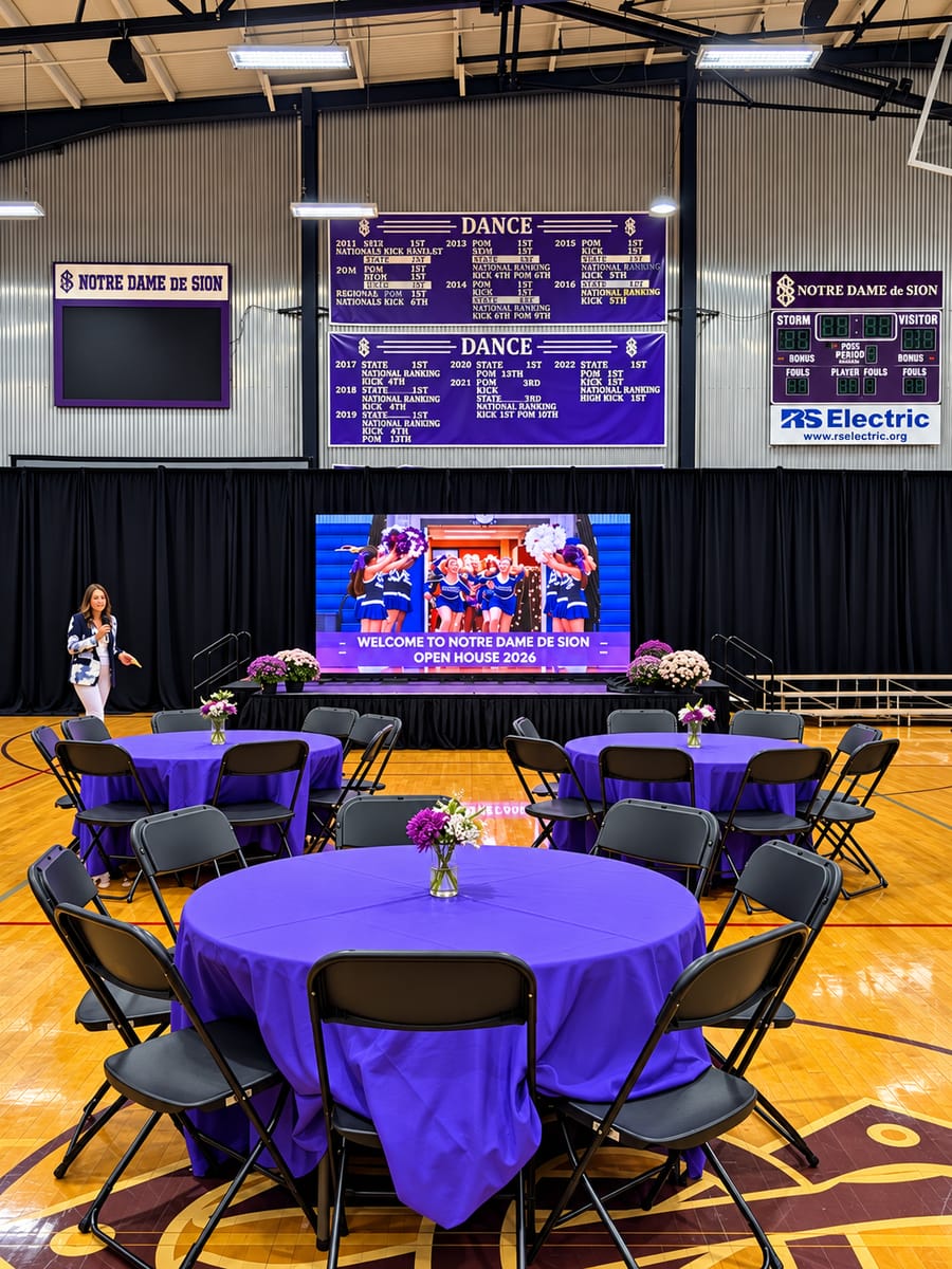 Round tables set in a school gym facing a Showtime LED wall on stage welcoming guests to an open house